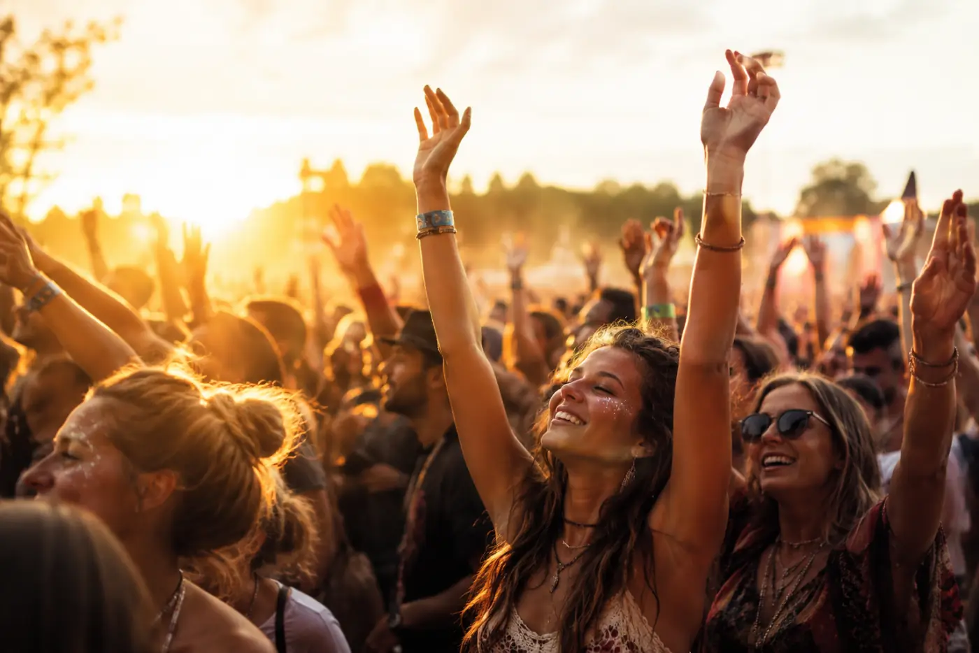 Público de braços erguidos em um festival ao entardecer, luz dourada e clima de celebração